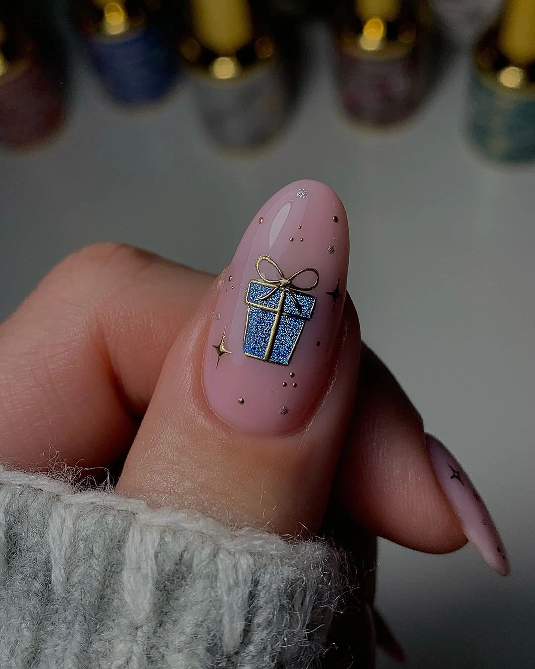 Pale pink almond nail with blue sparkling gift and gold-toned details