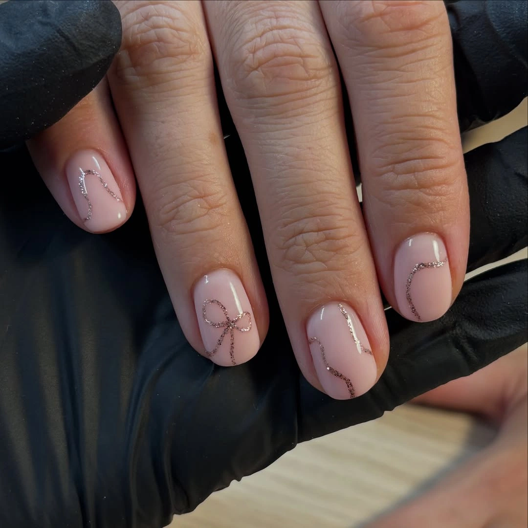 Short nude-pink nails with fine glitter lines and bow detail