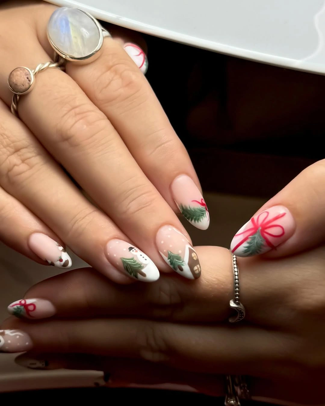 Short oval cream nails with red bow, evergreen trees, and branches
