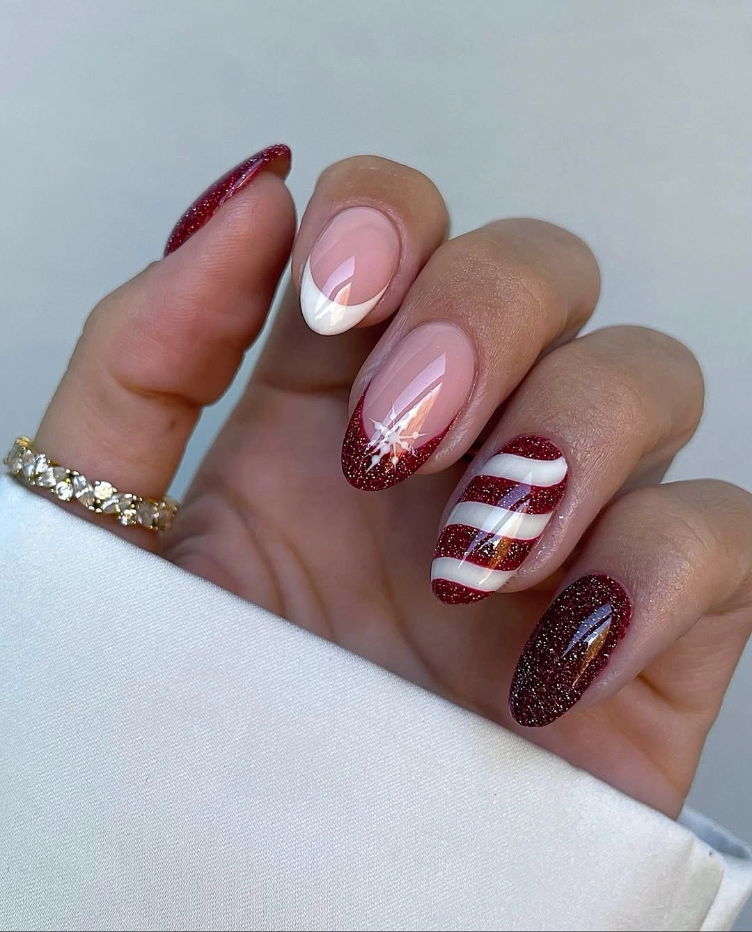 Almond nails with red glitter, white curves, stripes, and snowflake detail