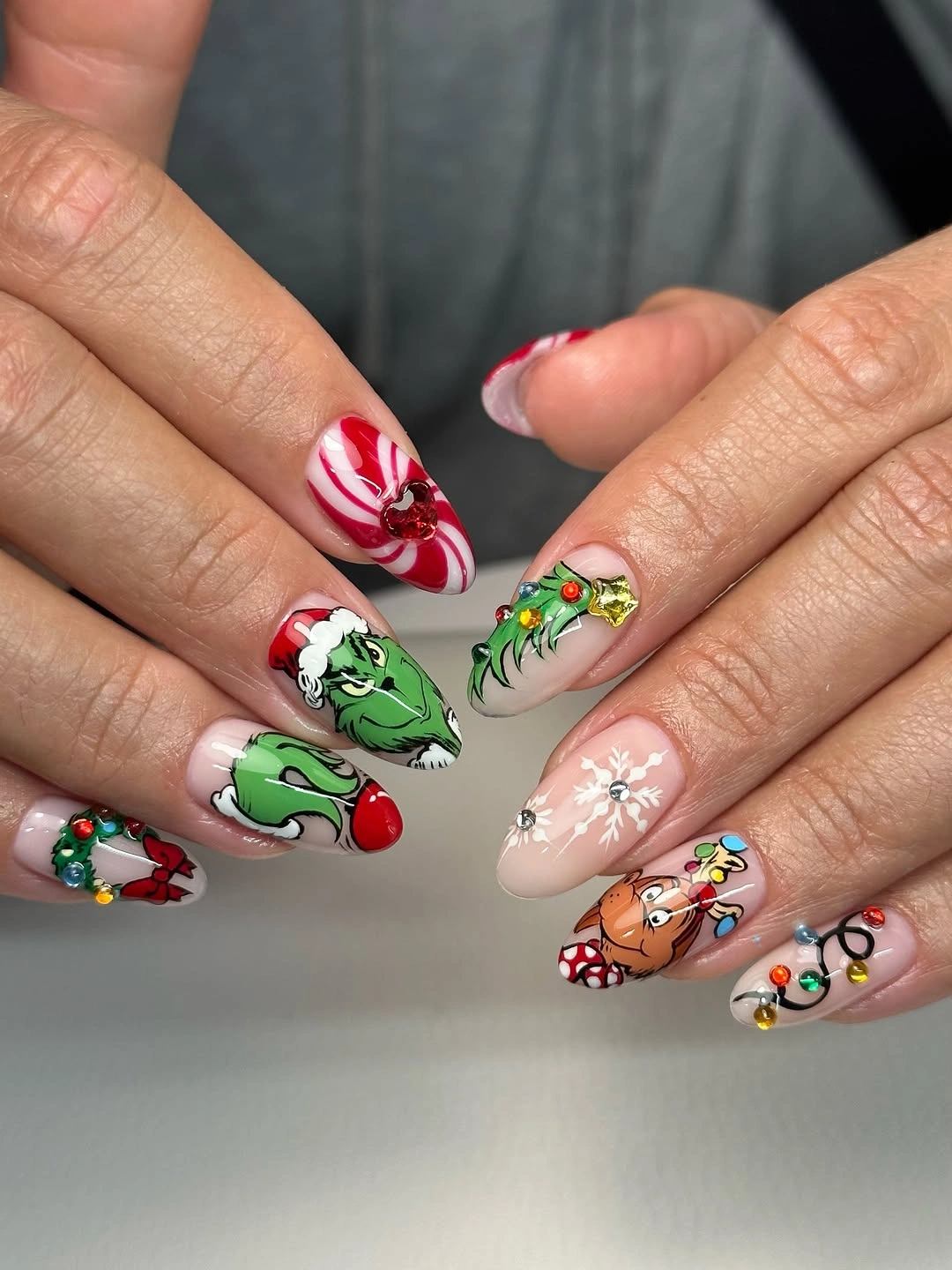 Almond nails with green cartoon face, reindeer, stripes, lights, and snowflakes