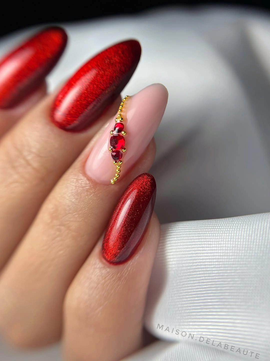 Long almond red shimmer nails with nude accent and ruby-like decorations