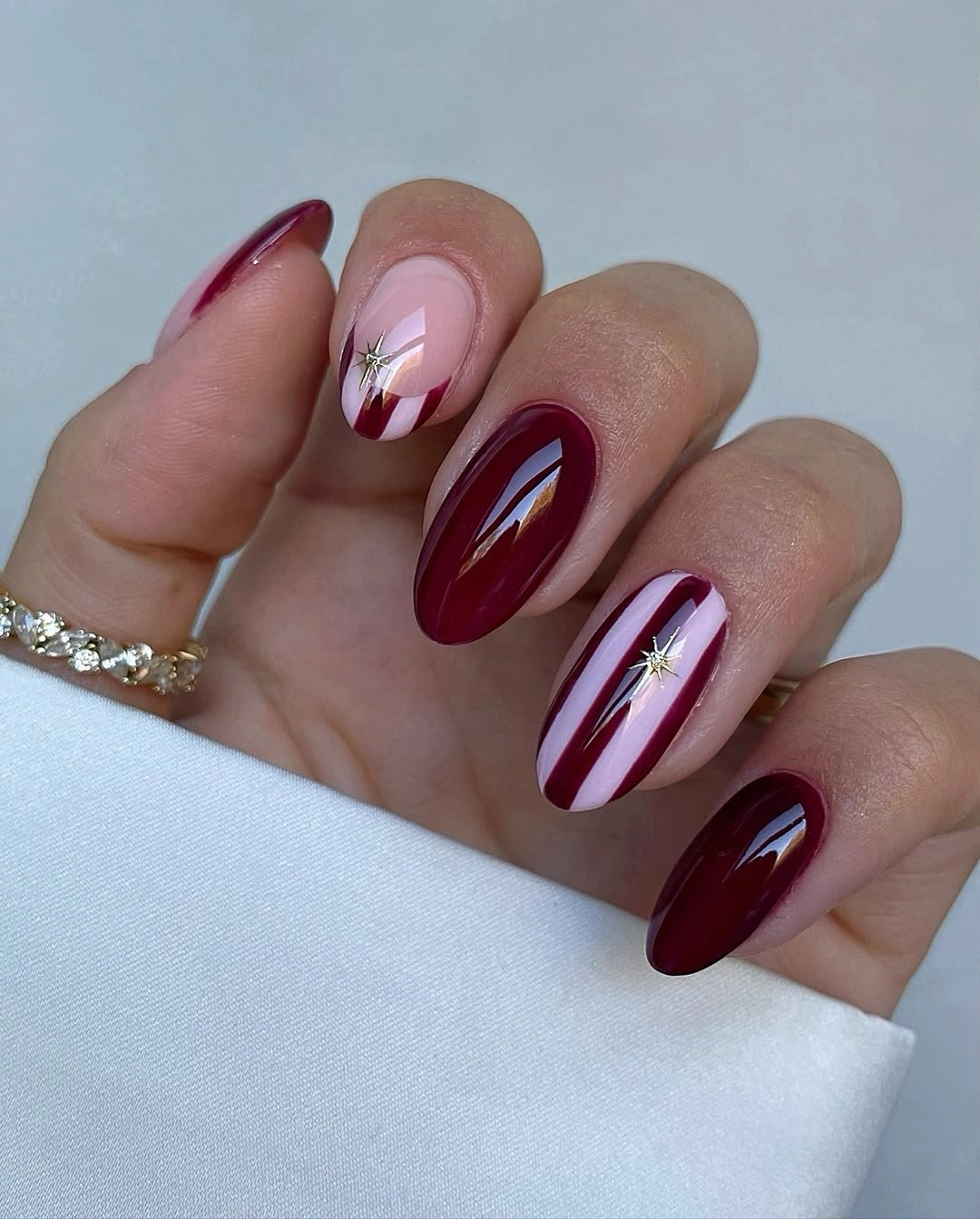 Glossy burgundy almond nails with pink bases and diagonal candy cane stripes
