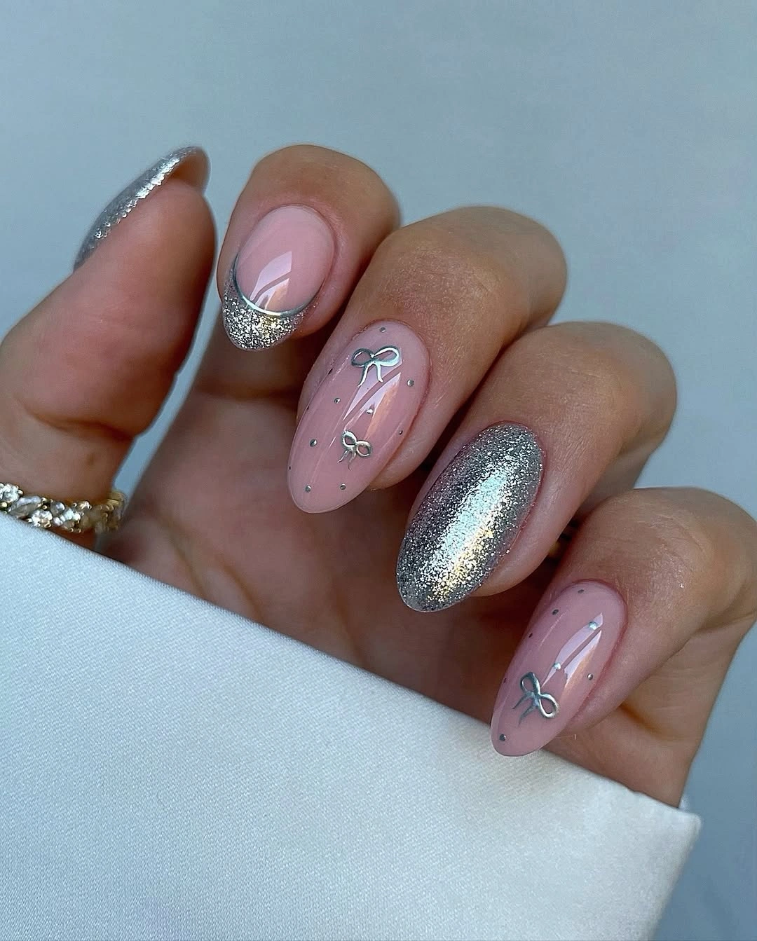 Pink almond nails with silver glitter accents and small silver bow designs
